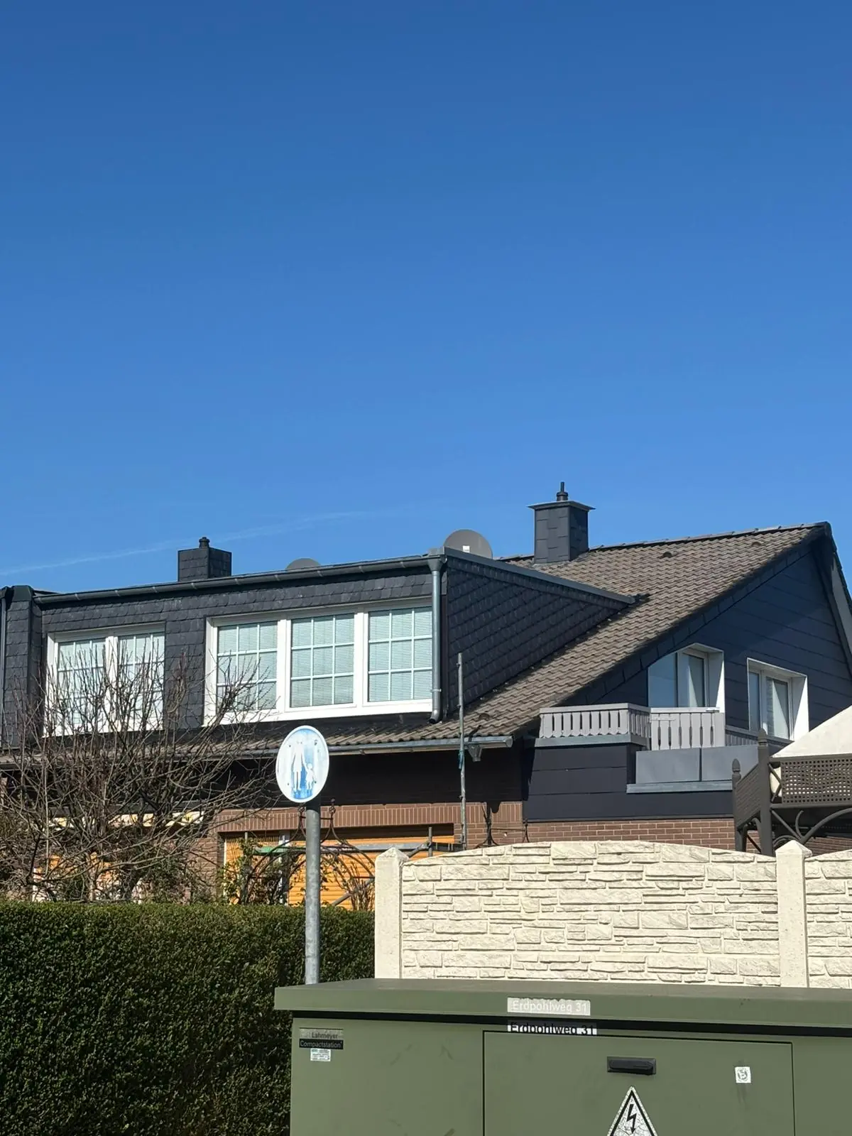 Vorher-Ansicht einer professionellen Dachreinigung in NRW: Ein Backsteinhaus mit stark vermoostem und wettergegerbtem Ziegeldach vor der Sanierung durch Brand Sanierungen.